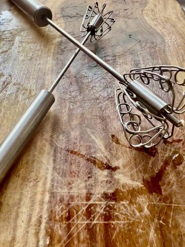 Handheld push whisks with beaters on wooden surface.