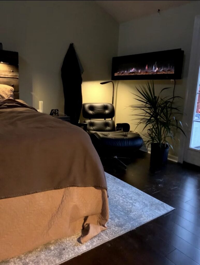 Cozy bedroom with modern electric fireplace, black lounge chair, and indoor plant.