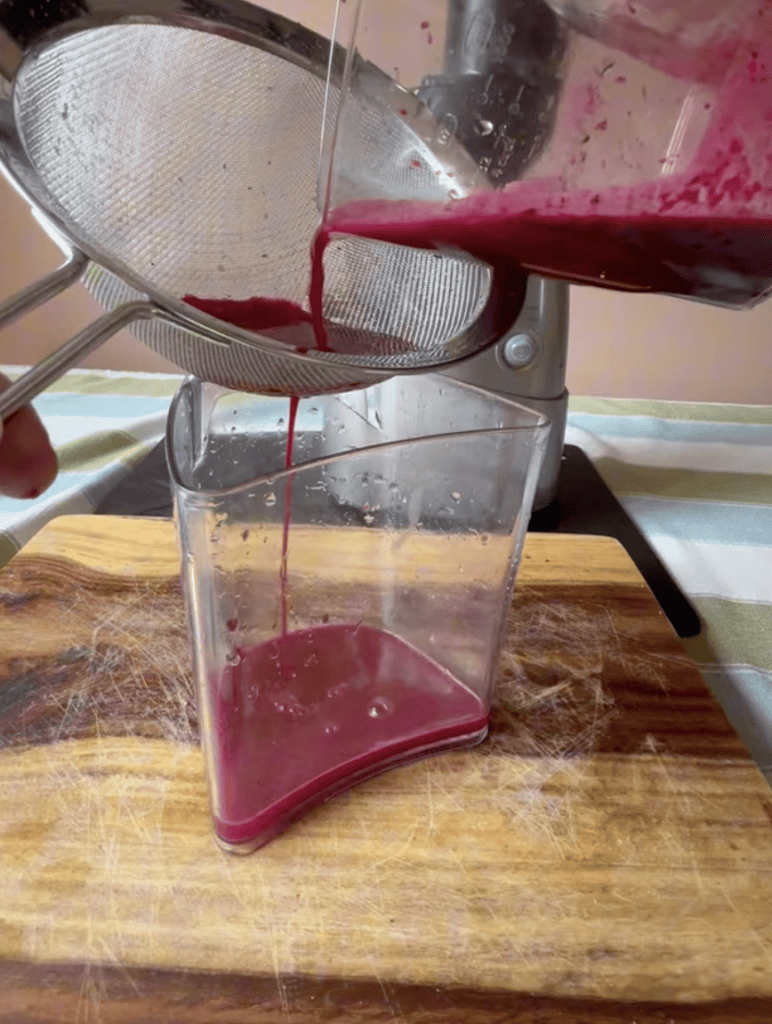 Straining deep purple juice through a fine mesh into a measuring cup.
