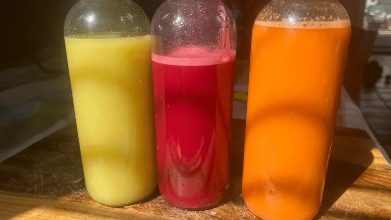 Three colorful juices in bottles on a wooden table.