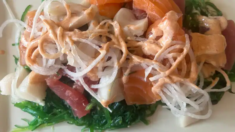 Seaweed salad with sashimi, spicy mayo, and vegetables on a white plate.