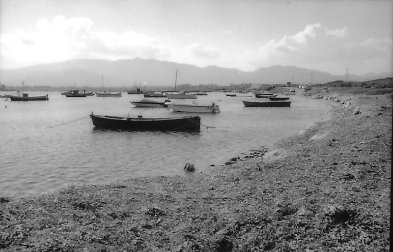 Boats anchored along a calm shoreline with mountains in the background.