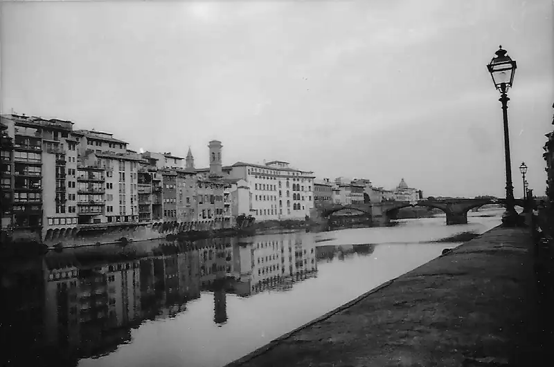 Historic black and white photo of Florence, Italy, with buildings along the riverbank.