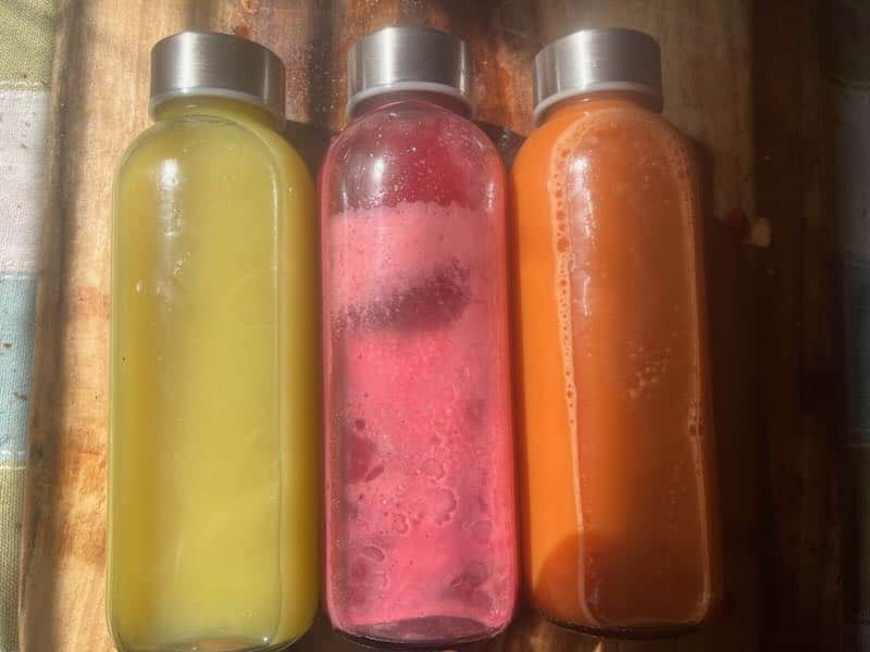 Three juice bottles from Redcypress Designs in yellow, pink, and orange blends.