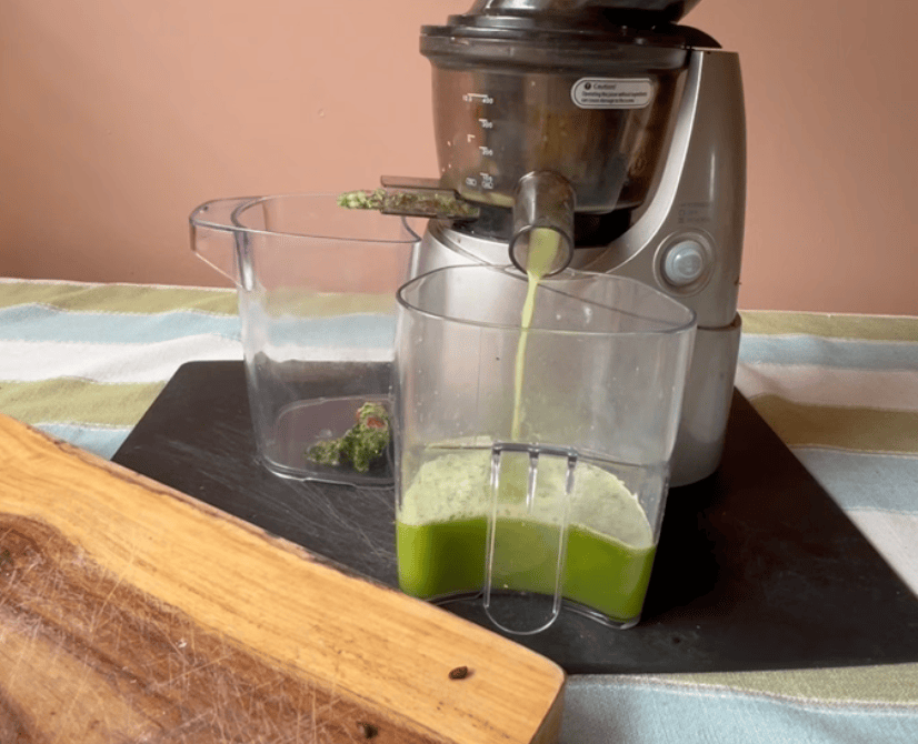 Fresh green juice pouring from juicer into glass container.