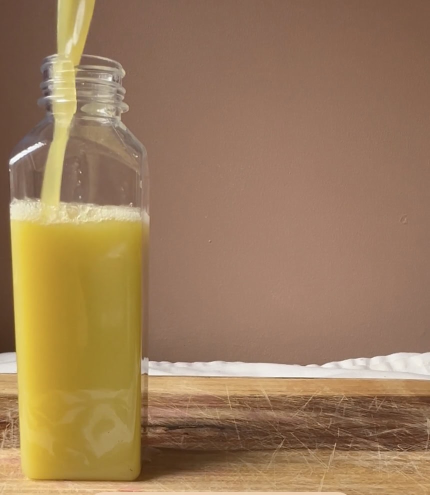 Glass bottle with yellow juice and straw on wooden surface.