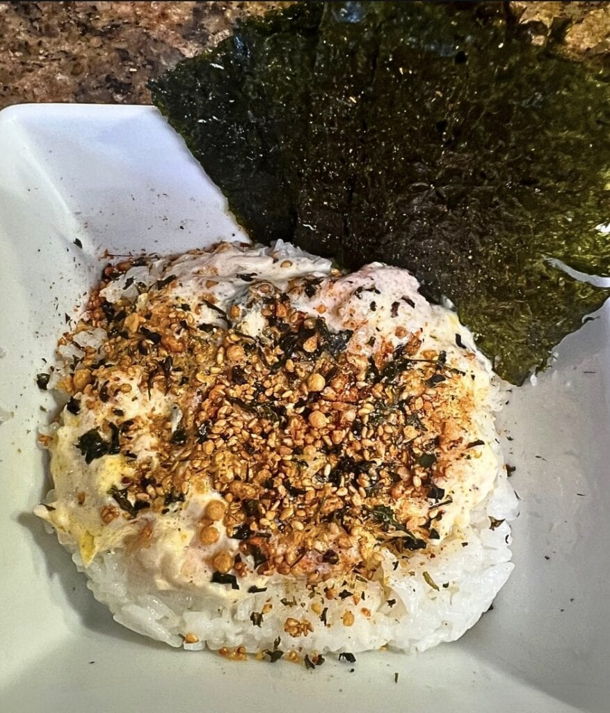 Close-up of rice topped with crunchy garlic and seaweed in a white bowl.