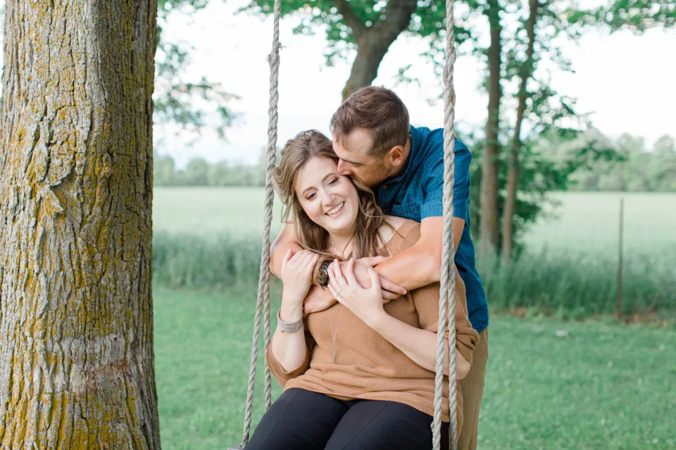 Swing between Trees - Engagement Session - Cow - Engagement Session Must Have Shot - Cows during Engagement Session - Poses during Engagement Session  Sunset - Natural Posing for Photo Session - Couples Photo Session Fun - Fun on the Farm - Farm Engagement Session - Blue and Brown Engagement Session Inspiration - Natural Engagement Session Posing - Ideas for what to wear for Engagement Photography, Modern Engagement Session Inspiration Wardrobe Ideas. Unsure of what to wear for your engagement photos, we've got you! Romantic brown with black leggings for Summer Engagement in Almonte. Grey Loft Studio is Ottawa's Wedding and Engagement Photographer for Real couples, showcasing photos that are modern, bright, and fun.