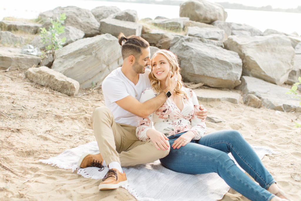 Sitting on the Beach - Ideas for what to wear for Engagement Photography, Modern Engagement Session Inspiration Wardrobe Ideas. Unsure of what to wear for your engagement photos, we've got you! Romantic floral shirt & jeans.  White T-shirt & neutral pants . Boat Shoes and Fancy. beaded sandals. Engagement at Petrie Island, Orleans. Grey Loft Studio is Ottawa's Wedding and Engagement Photographer Videographer for Real couples, showcasing photos that are modern, bright, and fun.