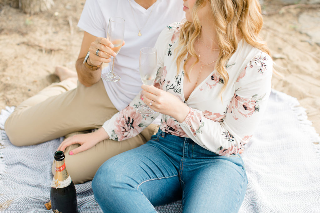 Romantic Shot - Sitting on the Beach - Ideas for what to wear for Engagement Photography, Modern Engagement Session Inspiration Wardrobe Ideas. Unsure of what to wear for your engagement photos, we've got you! Romantic floral shirt & jeans.  White T-shirt & neutral pants . Boat Shoes and Fancy. beaded sandals. Engagement at Petrie Island, Orleans. Grey Loft Studio is Ottawa's Wedding and Engagement Photographer Videographer for Real couples, showcasing photos that are modern, bright, and fun.