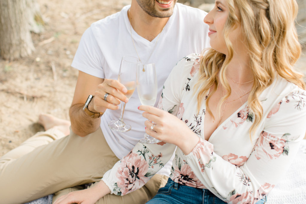 Romantic Shot - Sitting on the Beach - Ideas for what to wear for Engagement Photography, Modern Engagement Session Inspiration Wardrobe Ideas. Unsure of what to wear for your engagement photos, we've got you! Romantic floral shirt & jeans.  White T-shirt & neutral pants . Boat Shoes and Fancy. beaded sandals. Engagement at Petrie Island, Orleans. Grey Loft Studio is Ottawa's Wedding and Engagement Photographer Videographer for Real couples, showcasing photos that are modern, bright, and fun.