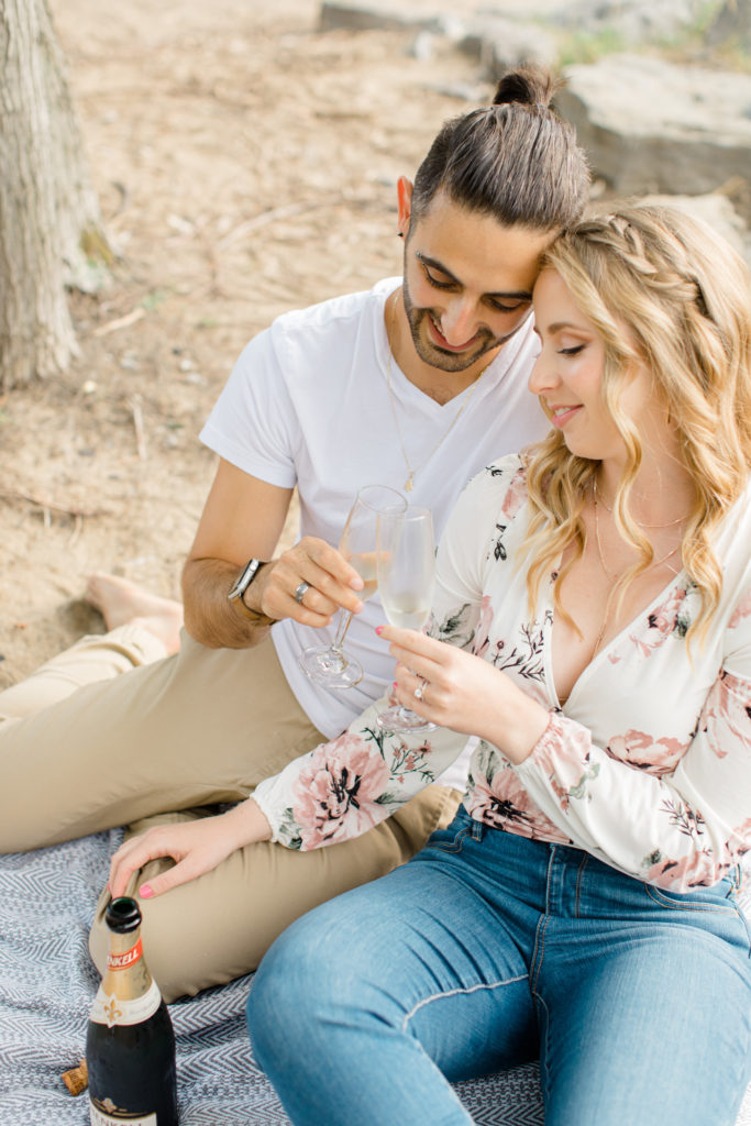 Romantic Shot - Sitting on the Beach - Ideas for what to wear for Engagement Photography, Modern Engagement Session Inspiration Wardrobe Ideas. Unsure of what to wear for your engagement photos, we've got you! Romantic floral shirt & jeans.  White T-shirt & neutral pants . Boat Shoes and Fancy. beaded sandals. Engagement at Petrie Island, Orleans. Grey Loft Studio is Ottawa's Wedding and Engagement Photographer Videographer for Real couples, showcasing photos that are modern, bright, and fun.