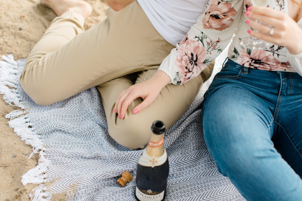 Hand on Leg - Sitting on the Beach - Ideas for what to wear for Engagement Photography, Modern Engagement Session Inspiration Wardrobe Ideas. Unsure of what to wear for your engagement photos, we've got you! Romantic floral shirt & jeans.  White T-shirt & neutral pants . Boat Shoes and Fancy. beaded sandals. Engagement at Petrie Island, Orleans. Grey Loft Studio is Ottawa's Wedding and Engagement Photographer Videographer for Real couples, showcasing photos that are modern, bright, and fun.