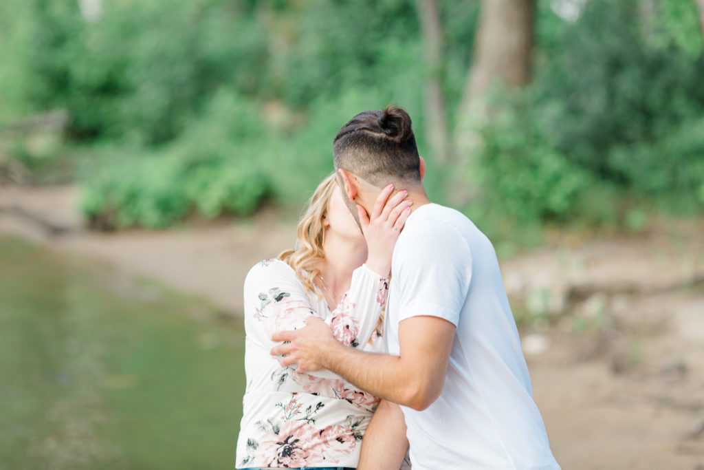 Kissing on the Beach - Ideas for what to wear for Engagement Photography, Modern Engagement Session Inspiration Wardrobe Ideas. Unsure of what to wear for your engagement photos, we've got you! Romantic floral shirt & jeans.  White T-shirt & neutral pants . Boat Shoes and Fancy. beaded sandals. Engagement at Petrie Island, Orleans. Grey Loft Studio is Ottawa's Wedding and Engagement Photographer Videographer for Real couples, showcasing photos that are modern, bright, and fun.