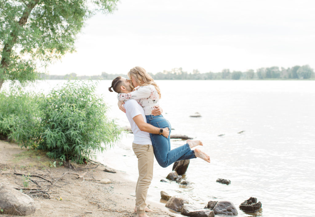Lifting on the beach - Ideas for what to wear for Engagement Photography, Modern Engagement Session Inspiration Wardrobe Ideas. Unsure of what to wear for your engagement photos, we've got you! Romantic floral shirt & jeans.  White T-shirt & neutral pants . Boat Shoes and Fancy. beaded sandals. Engagement at Petrie Island, Orleans. Grey Loft Studio is Ottawa's Wedding and Engagement Photographer Videographer for Real couples, showcasing photos that are modern, bright, and fun.