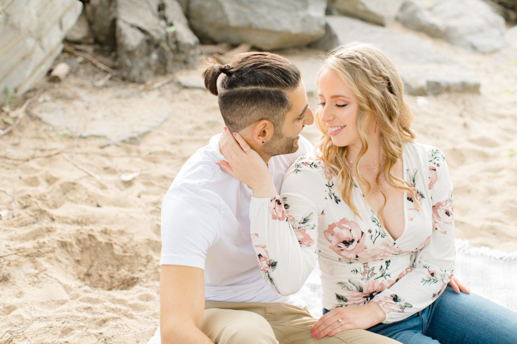 Romantic Pose - Sitting on the Beach - Ideas for what to wear for Engagement Photography, Modern Engagement Session Inspiration Wardrobe Ideas. Unsure of what to wear for your engagement photos, we've got you! Romantic floral shirt & jeans.  White T-shirt & neutral pants . Boat Shoes and Fancy. beaded sandals. Engagement at Petrie Island, Orleans. Grey Loft Studio is Ottawa's Wedding and Engagement Photographer Videographer for Real couples, showcasing photos that are modern, bright, and fun.