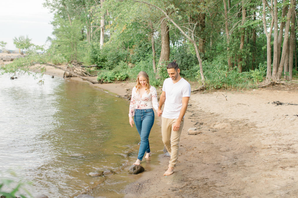 Walking on the beach - Ideas for what to wear for Engagement Photography, Modern Engagement Session Inspiration Wardrobe Ideas. Unsure of what to wear for your engagement photos, we've got you! Romantic floral shirt & jeans.  White T-shirt & neutral pants . Boat Shoes and Fancy. beaded sandals. Engagement at Petrie Island, Orleans. Grey Loft Studio is Ottawa's Wedding and Engagement Photographer Videographer for Real couples, showcasing photos that are modern, bright, and fun.