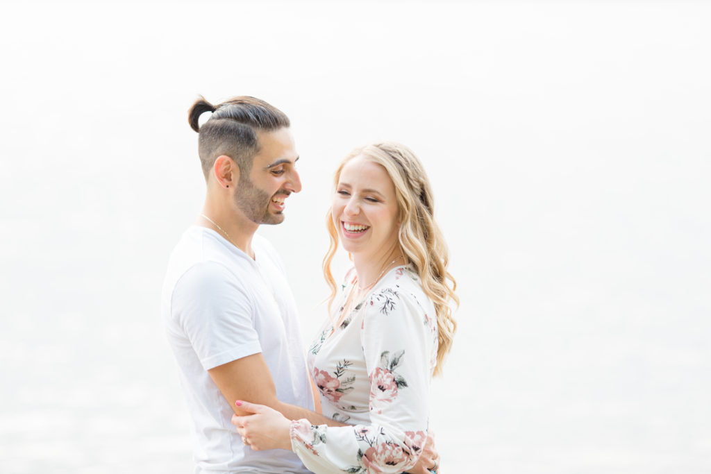 Cute Poses on the beach - Ideas for what to wear for Engagement Photography, Modern Engagement Session Inspiration Wardrobe Ideas. Unsure of what to wear for your engagement photos, we've got you! Romantic floral shirt & jeans.  White T-shirt & neutral pants . Boat Shoes and Fancy. beaded sandals. Engagement at Petrie Island, Orleans. Grey Loft Studio is Ottawa's Wedding and Engagement Photographer Videographer for Real couples, showcasing photos that are modern, bright, and fun.