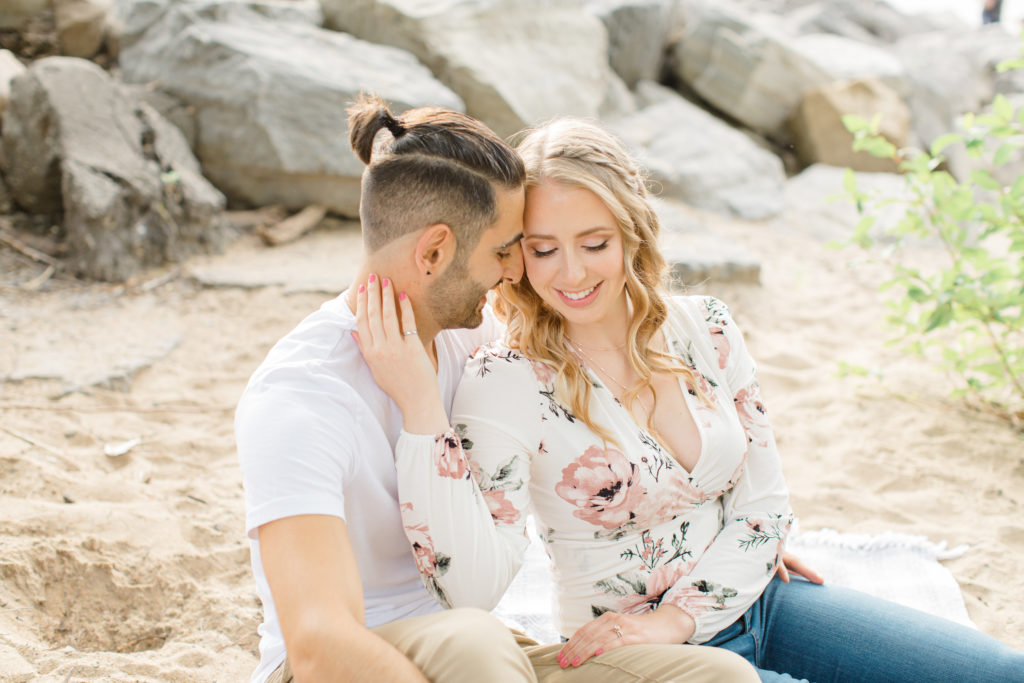 Romantic Pose - Sitting on the Beach - Ideas for what to wear for Engagement Photography, Modern Engagement Session Inspiration Wardrobe Ideas. Unsure of what to wear for your engagement photos, we've got you! Romantic floral shirt & jeans.  White T-shirt & neutral pants . Boat Shoes and Fancy. beaded sandals. Engagement at Petrie Island, Orleans. Grey Loft Studio is Ottawa's Wedding and Engagement Photographer Videographer for Real couples, showcasing photos that are modern, bright, and fun.