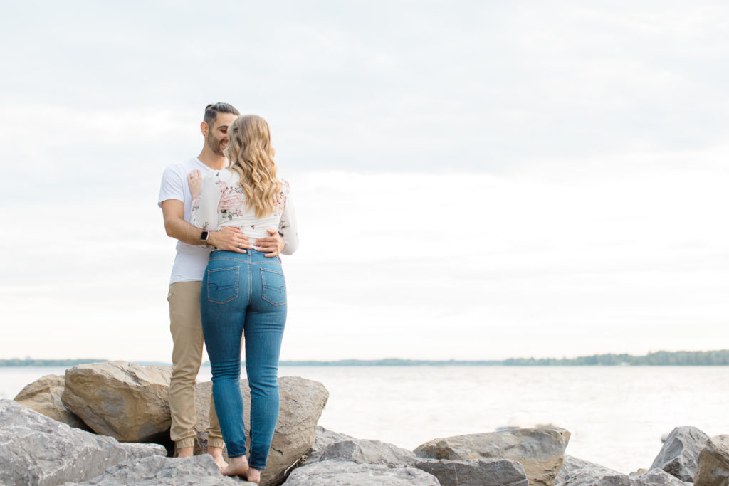 Cute Poses on the beach - Ideas for what to wear for Engagement Photography, Modern Engagement Session Inspiration Wardrobe Ideas. Unsure of what to wear for your engagement photos, we've got you! Romantic floral shirt & jeans.  White T-shirt & neutral pants . Boat Shoes and Fancy. beaded sandals. Engagement at Petrie Island, Orleans. Grey Loft Studio is Ottawa's Wedding and Engagement Photographer Videographer for Real couples, showcasing photos that are modern, bright, and fun.
