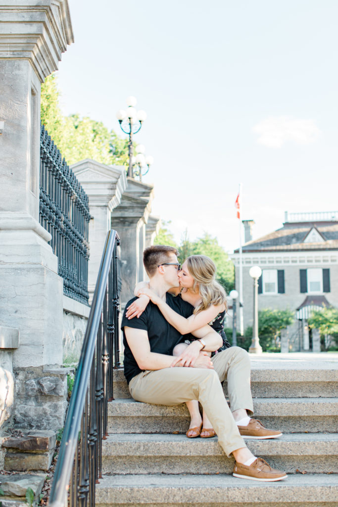 Cute couple Posing while sitting on steps at Rideau Hall - Ideas for what to wear for Engagement Photography, Modern Engagement Session Inspiration Wardrobe Ideas. Unsure of what to wear for your engagement photos, we've got you! Romantic floral dress. Black Polo T-shirt & neutral pants . Boat Shoes and Fancy beaded wedges. Engagement downtown Ottawa. Grey Loft Studio is Ottawa's Wedding and Engagement Photographer Videographer for Real couples, showcasing photos that are modern, bright, and fun.