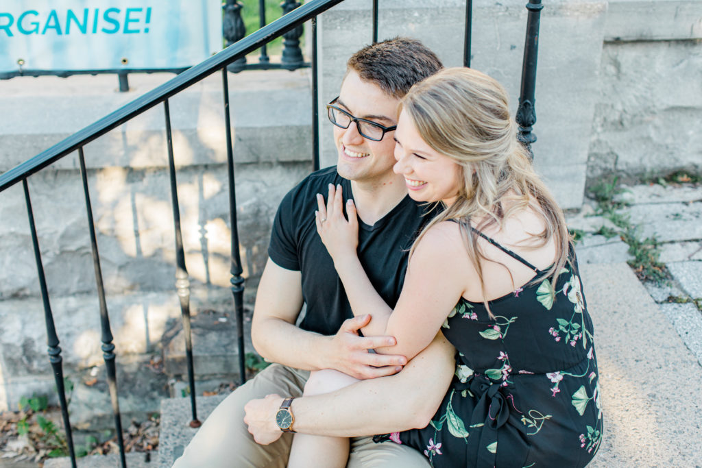 Engagement Session Hair Inspiration - Cute couple Posing while sitting on steps at Rideau Hall - Ideas for what to wear for Engagement Photography, Modern Engagement Session Inspiration Wardrobe Ideas. Unsure of what to wear for your engagement photos, we've got you! Romantic floral dress. Black Polo T-shirt & neutral pants . Boat Shoes and Fancy beaded wedges. Engagement downtown Ottawa. Grey Loft Studio is Ottawa's Wedding and Engagement Photographer Videographer for Real couples, showcasing photos that are modern, bright, and fun.
