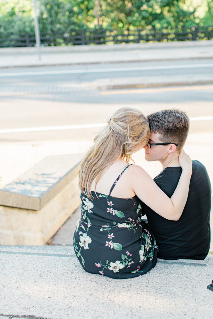 Engagement Photo Poses- Cute couple Posing while sitting on steps at Rideau Hall - Ideas for what to wear for Engagement Photography, Modern Engagement Session Inspiration Wardrobe Ideas. Unsure of what to wear for your engagement photos, we've got you! Romantic floral dress. Black Polo T-shirt & neutral pants . Boat Shoes and Fancy beaded wedges. Engagement downtown Ottawa. Grey Loft Studio is Ottawa's Wedding and Engagement Photographer Videographer for Real couples, showcasing photos that are modern, bright, and fun.