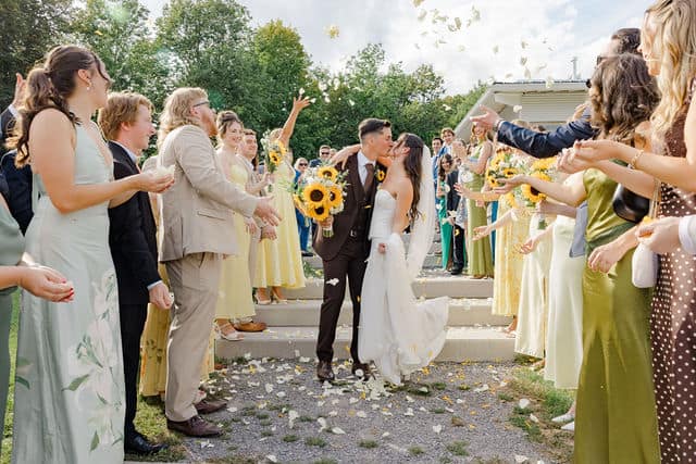 Wedding guests tossing flower petals as Julia and Will kiss on the steps