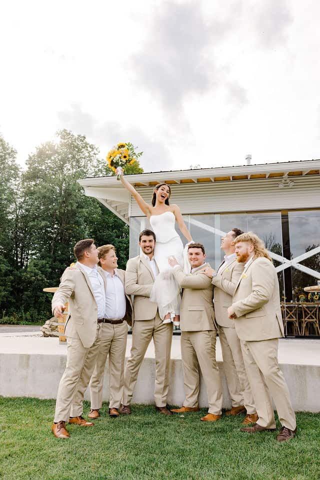 Groomsmen lifting the bride up to celebrate outside the cidery building