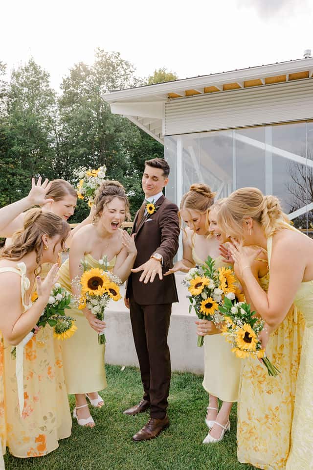 Bridesmaids in yellow dresses laughing together, with the cidery building in the background