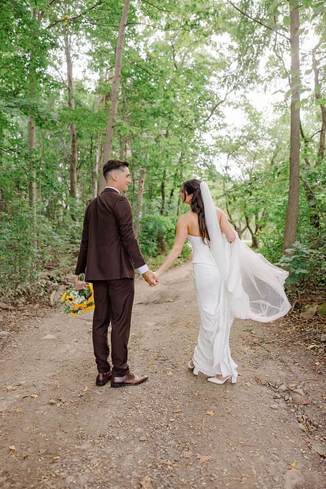 Julia and Will walking down a wooded path, her veil catching the breeze