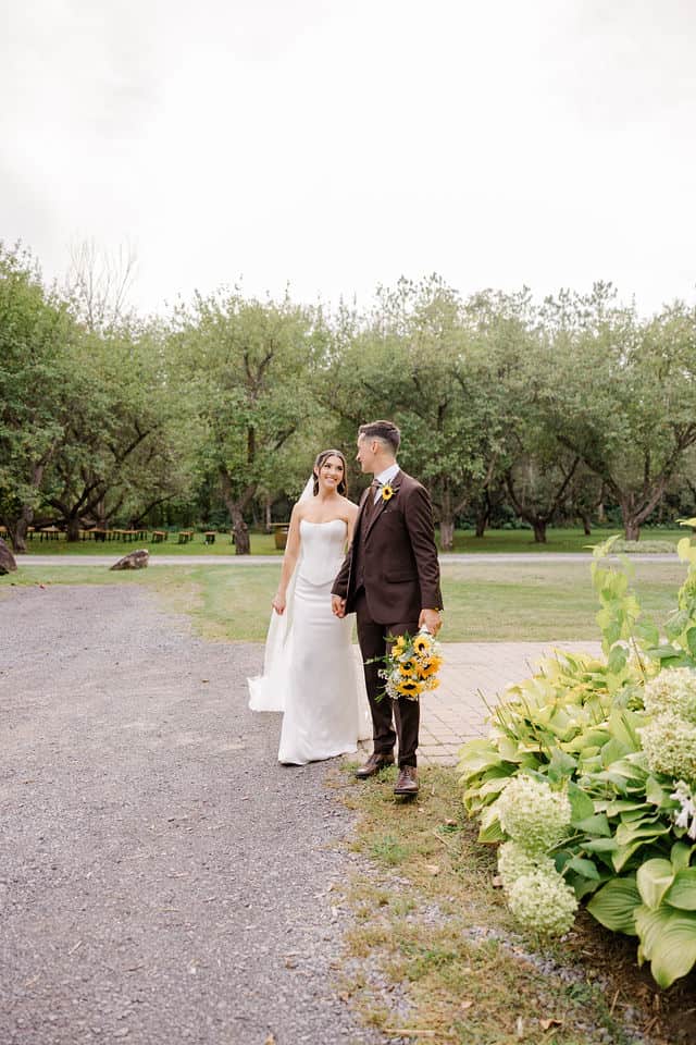 Julia and Will walking hand in hand through the orchard