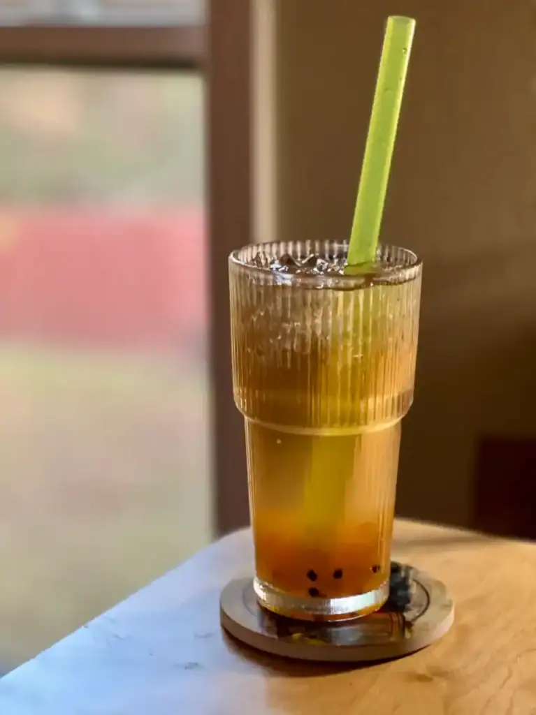 Refreshing bubble tea with green straw on wooden table.