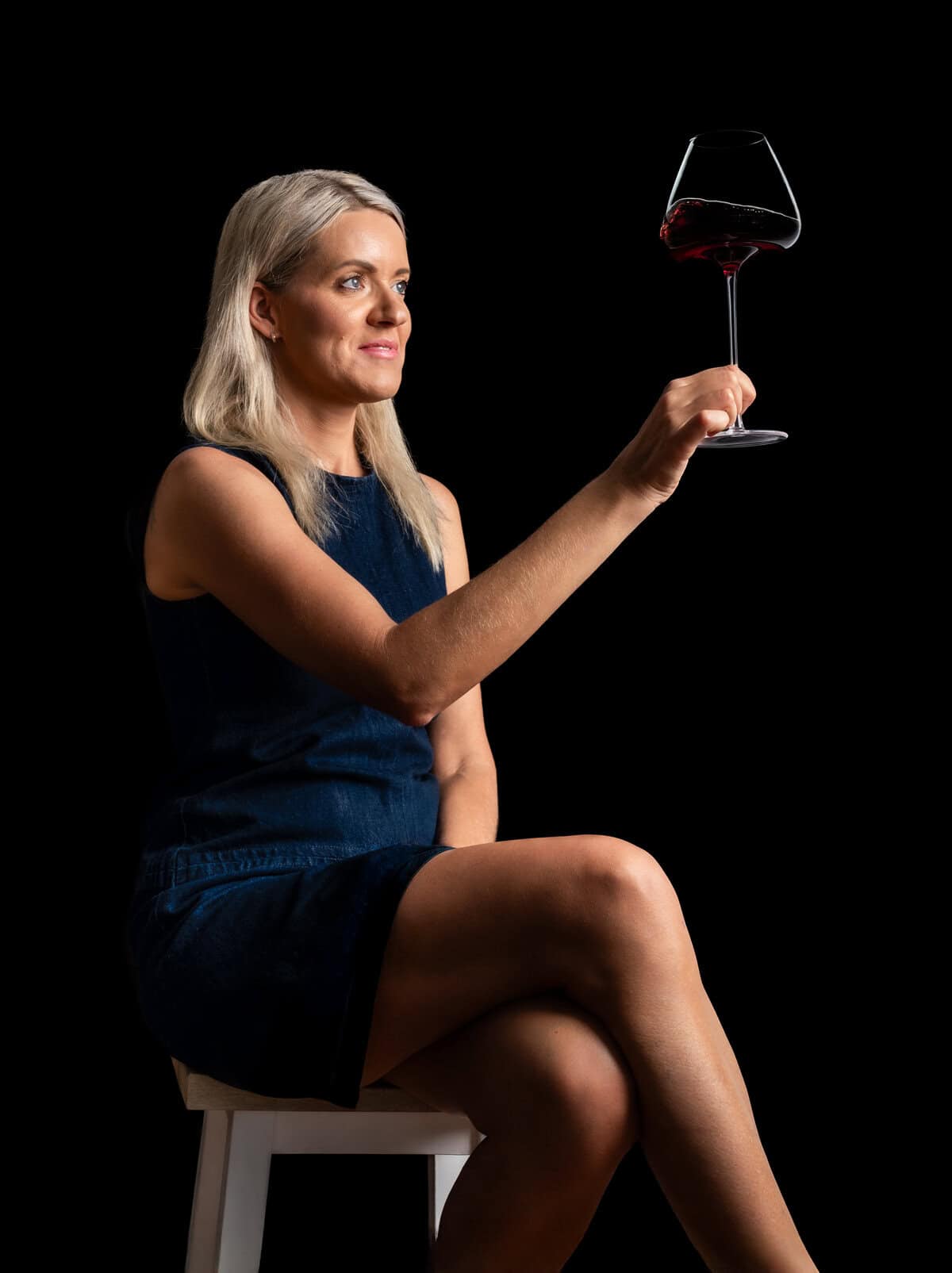 Elegant woman holding a glass of red wine against a black background.