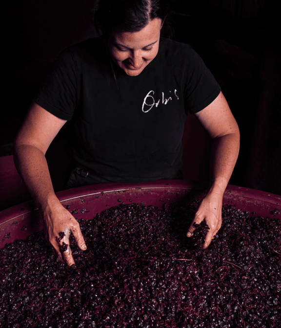 Woman enjoying wine tasting with grapes in a pink tub, close-up.