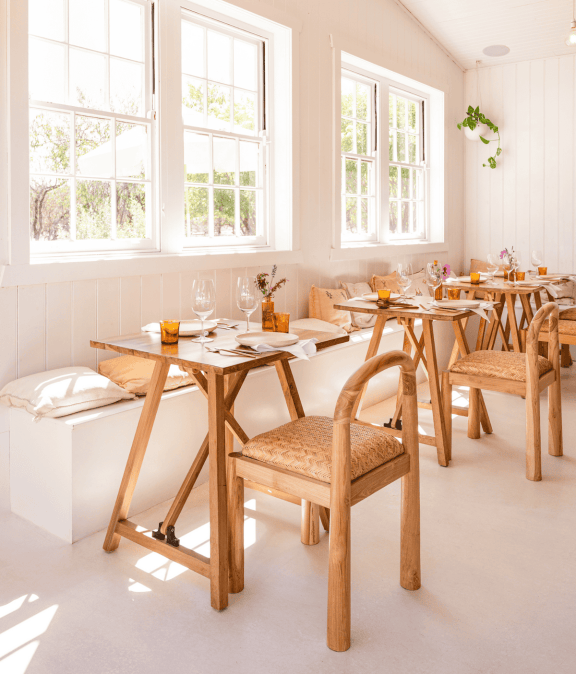 Bright, airy restaurant interior with wooden tables and chairs, large windows, and fresh decor.