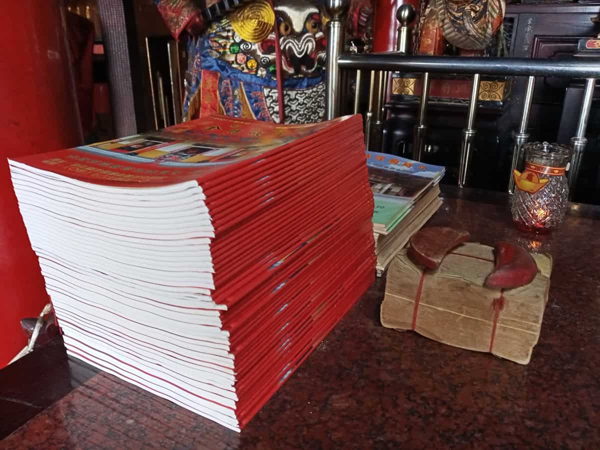 A stack of nongli lunar almanac booklets and joss papers at a temple — the printed calendar a festival year is read from.