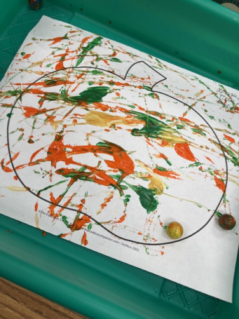 Photo of a pumpkin with marbles and paint spread across the pumpkin. Easy progressive art idea.
