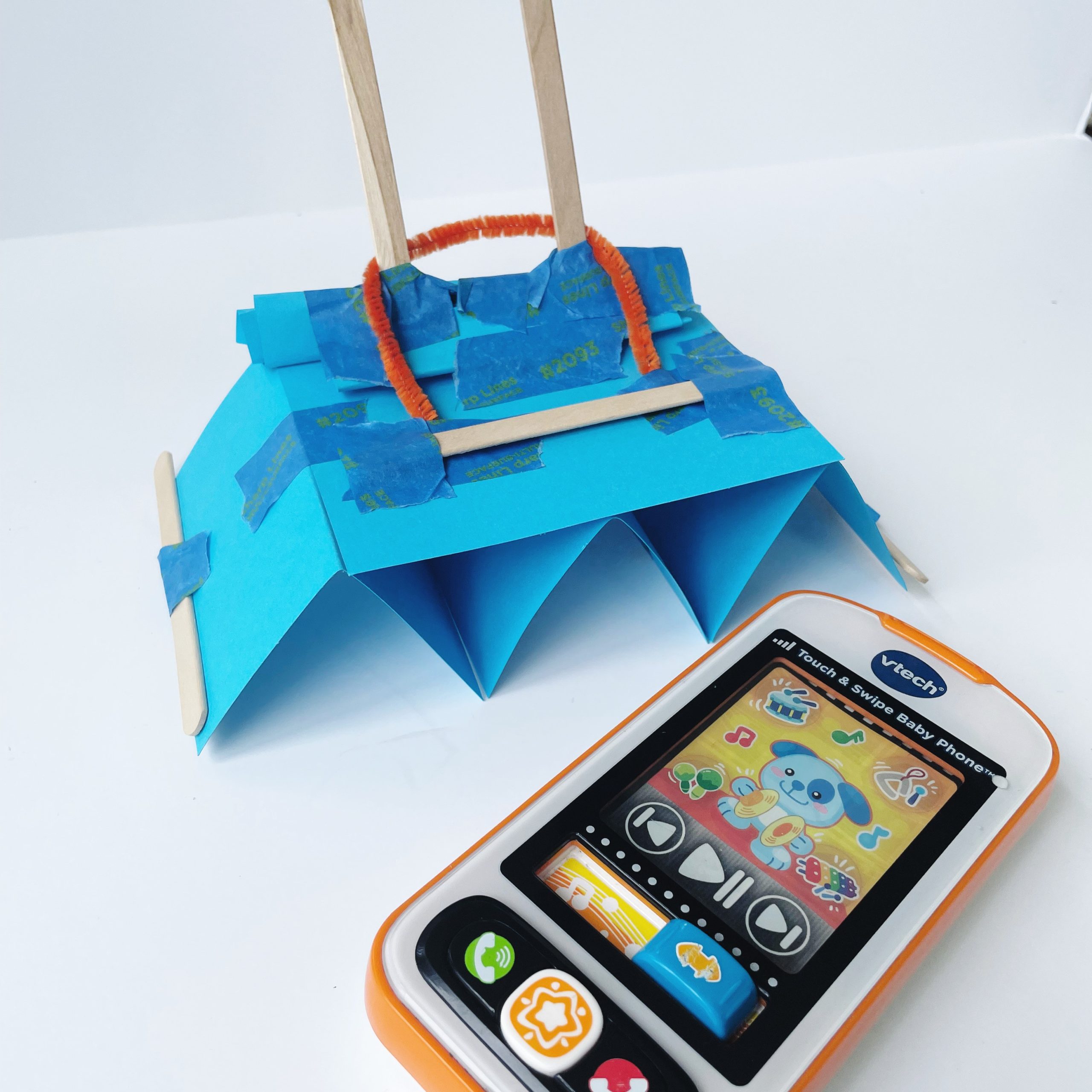 Vtech phone device on the table next to a complete handmade phone stand for engineering design project as part of a what is engineering lesson