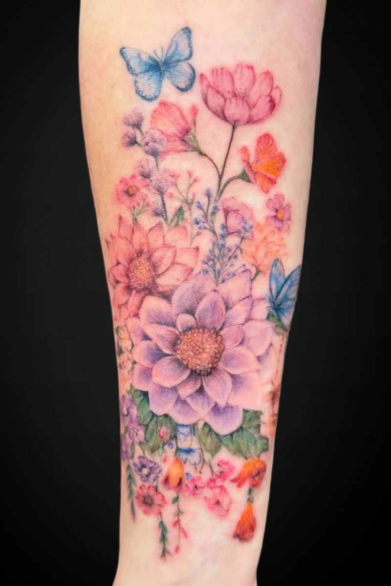 Colorful watercolor flower tattoo wrapping the forearm, with pink, purple, orange blooms and blue butterflies.