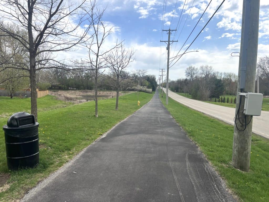Smooth paved bike trail along suburban neighborhood in Chicago with trees, green grass, and utility poles for cycling and outdoor recreation.