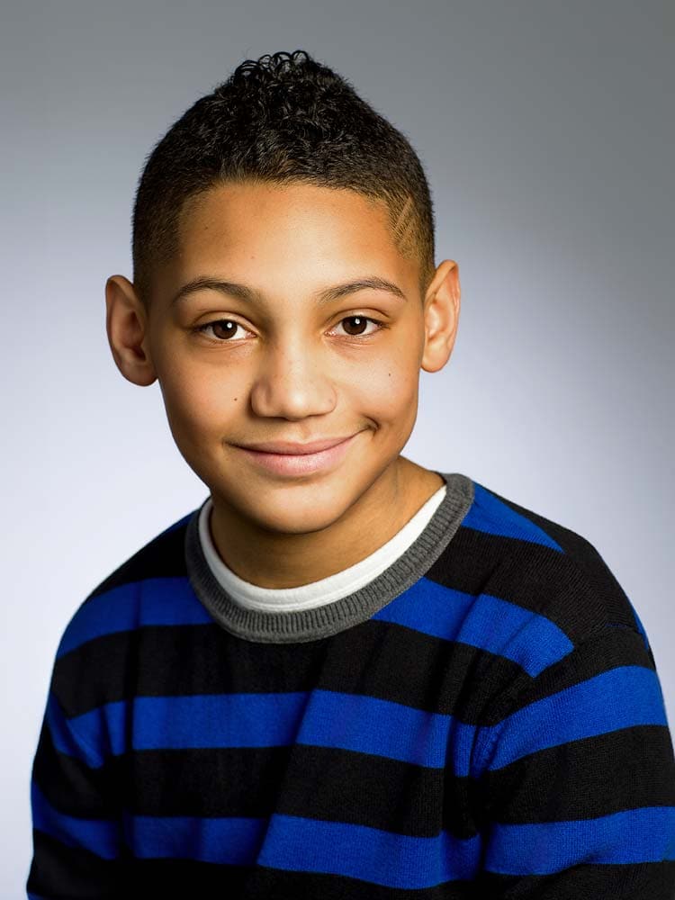 Bright young boy with a friendly smile in a Sussex headshot, wearing a blue and black striped sweater, professional portrait for personal or corporate branding.