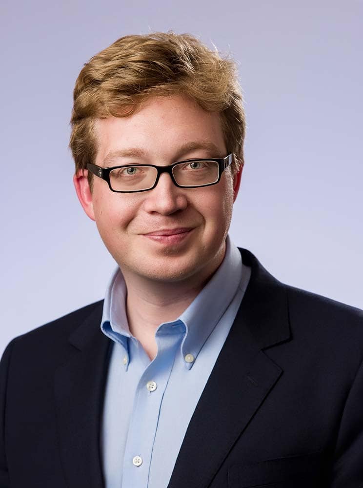 Professional headshot of a young businessman in Sussex, wearing glasses and a navy suit, perfect for corporate or LinkedIn profile images.