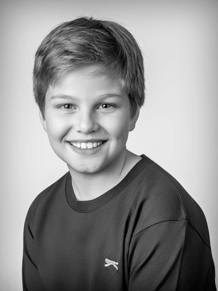 Bright young boy smiling in Sussex headshots, professional children's portrait photography, high-quality school photos, natural light, with a casual black sweatshirt, perfect for family or school portfolios.