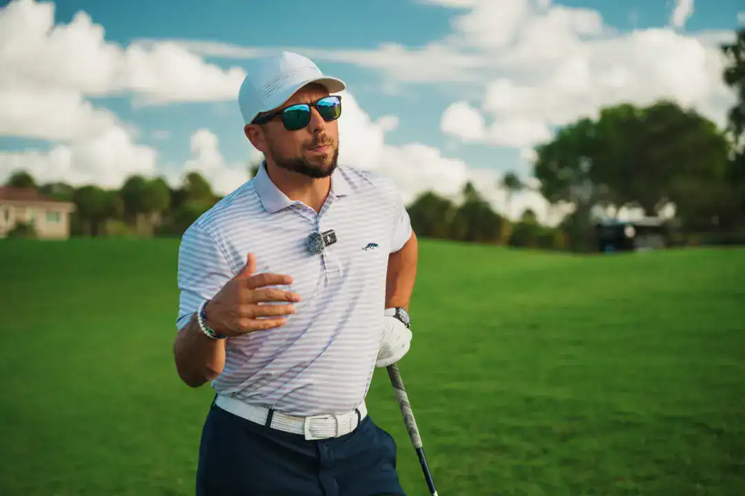 Man playing golf on a lush green course under a partly cloudy sky, wearing sunglasses and sporty attire, representing leisure and outdoor sports.