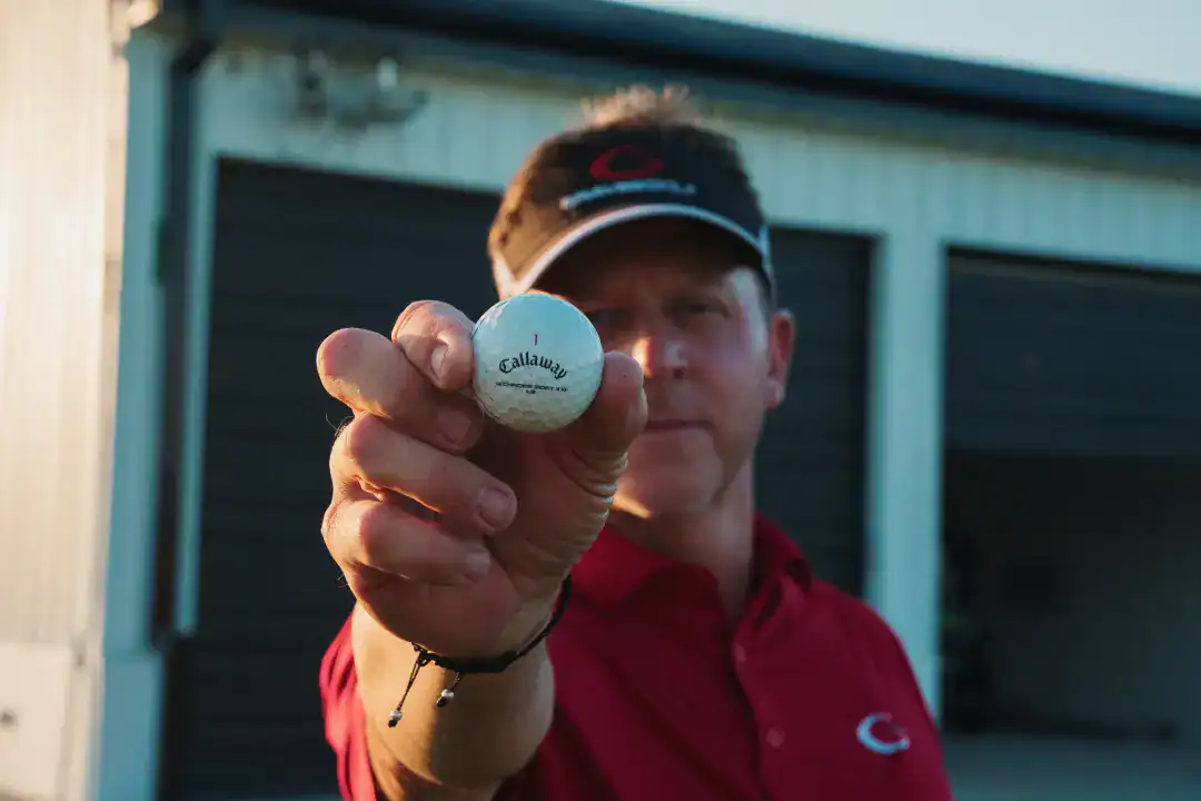 Callaway golf ball held by a man wearing a red polo shirt and a black visor in an outdoor setting.