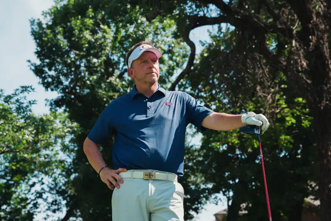 Experienced golfer standing on lush golf course, holding a golf club, showcasing professional golf attire and concentration.