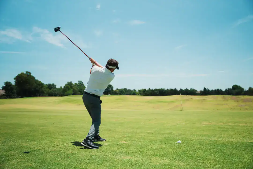 - Young man playing golf on a sunny course, practicing his swing with a golf club, lush green fairway, and blue sky, emphasizing outdoor sports, leisure, and golf event experiences.