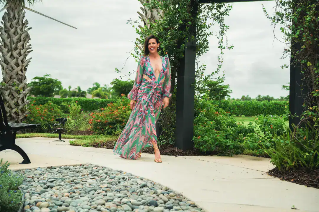 Vibrant woman in a colorful maxi dress walking outdoors in a lush, green garden setting, showcasing fashion, elegance, and lifestyle for Syslo Ventures.