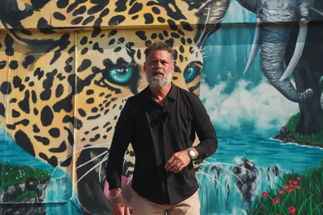 Vibrant jungle-themed graffiti mural featuring a detailed leopard face, waterfall, and lush greenery, with a man standing in front, representing urban art and creative expression.